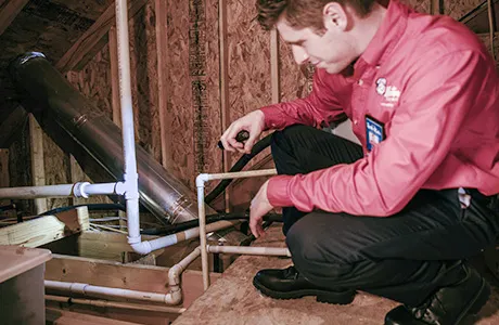 Mr. Rooter tech looking at pipes in an attic during a gas leak repair in Rochester, MN