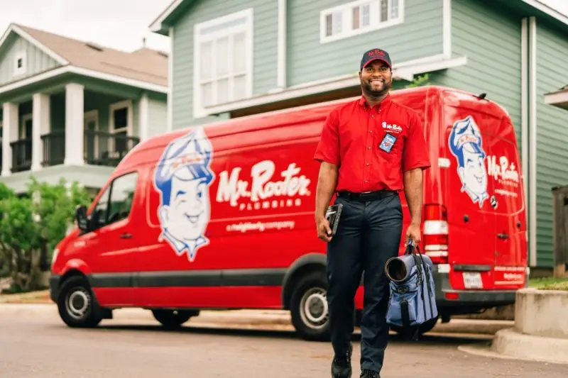 A courteous Mr. Rooter plumber holding a bag of tools and walking towards a home to perform a plumbing repair