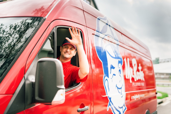 : Mr. Rooter plumber waving from a work van.