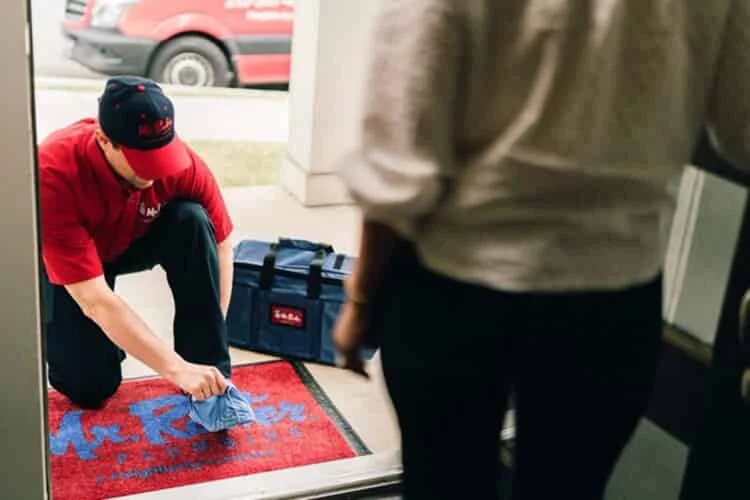 Mr. Rooter plumber bending down at customers' front door to put on shoe covers before starting plumbing work.