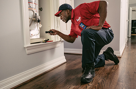 A Mr. Rooter plumber using a flash light to troubleshoot and indoor water heater