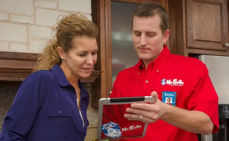 A plumber using an electronic tablet to show a woman information about sewer line replacement in San Antonio, TX.