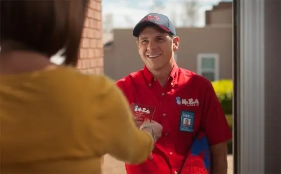 Smiling male Mr. Rooter employee handing business card to customer.