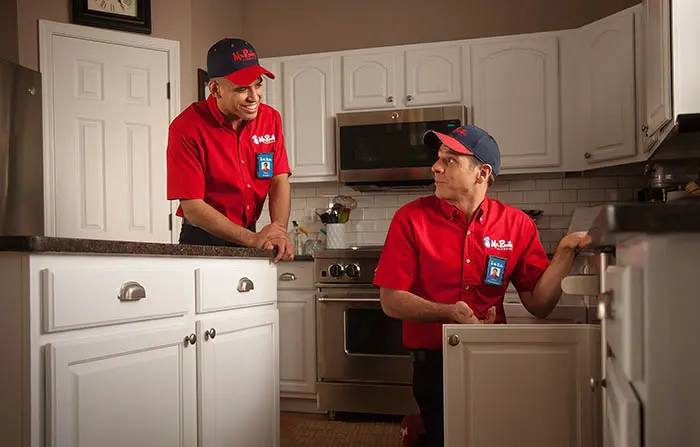 Pair of male Mr. Rooter technicians in residential kitchen.